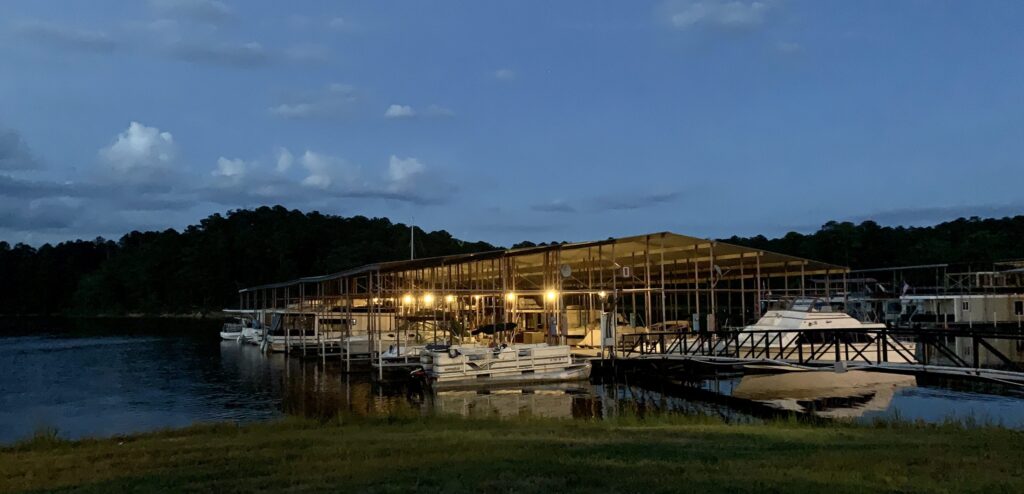 Illuminated boat slips and docks under a covered marina at dusk.